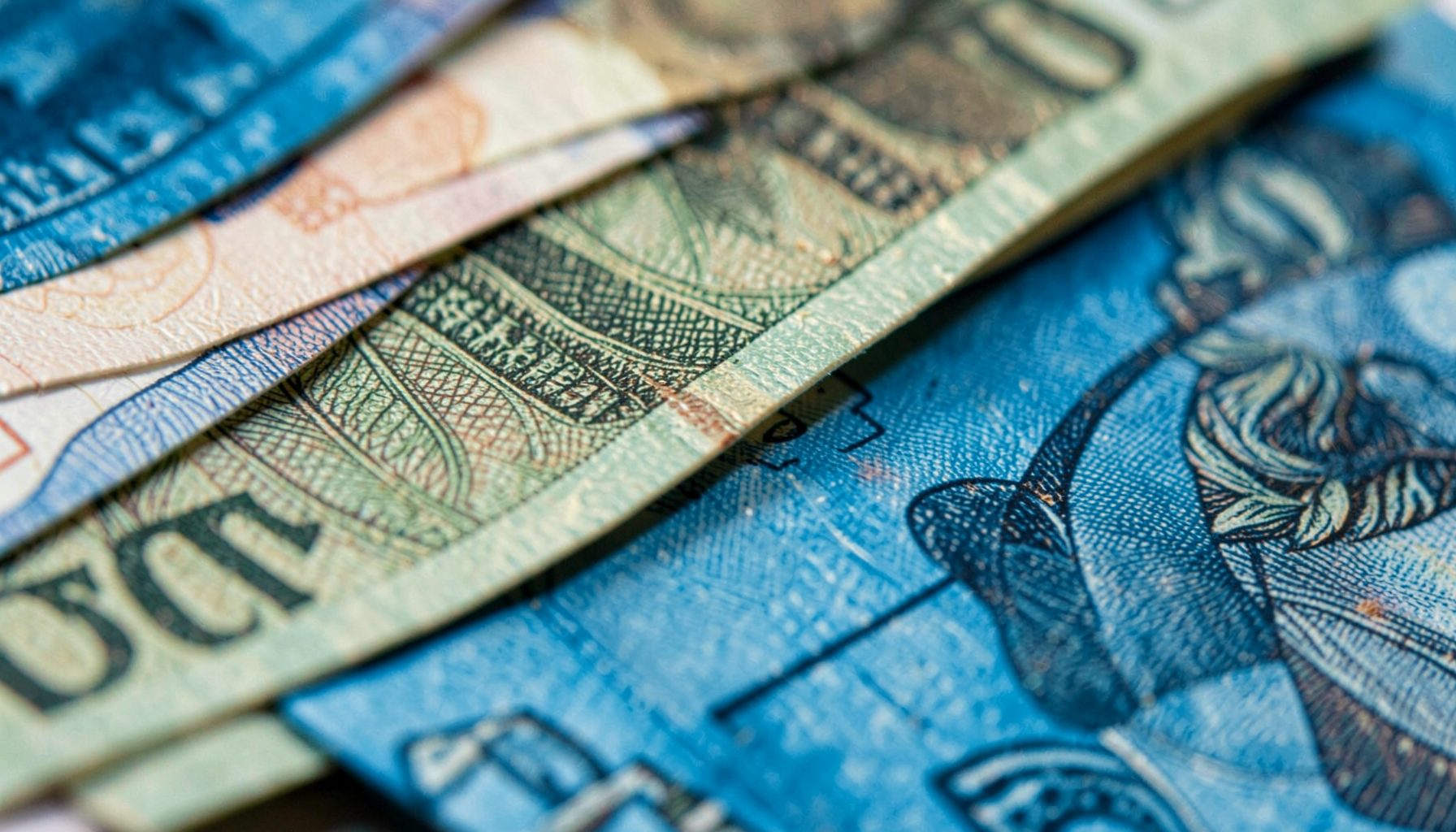 Extreme close-up photograph of textured Tanzanian shilling banknotes, layered and overlapping, with intricate engraved patterns
