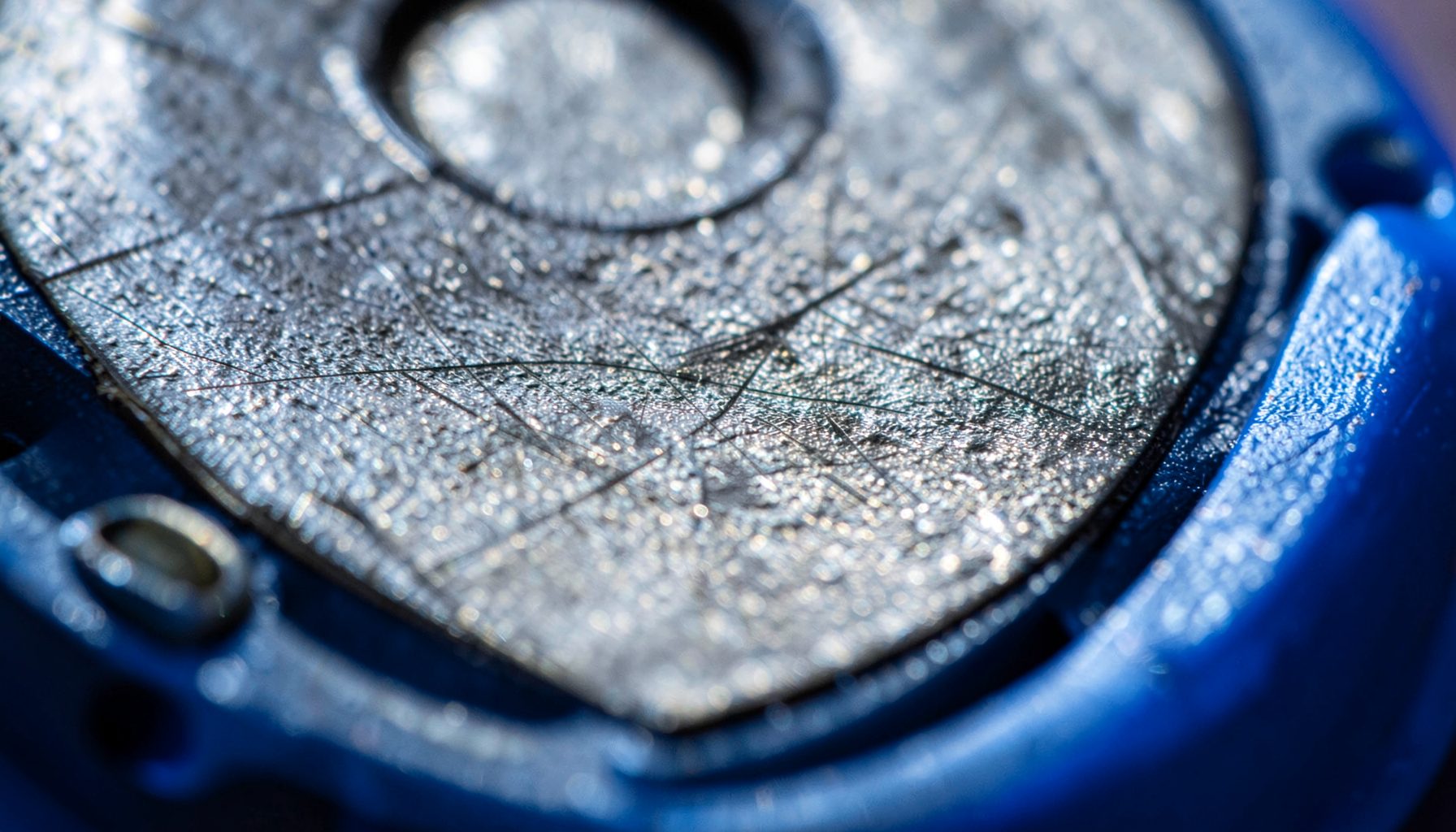 Extreme close-up photograph of worn, textured film reel surface with subtle metallic sheen and fine scratches, deep charcoal tones