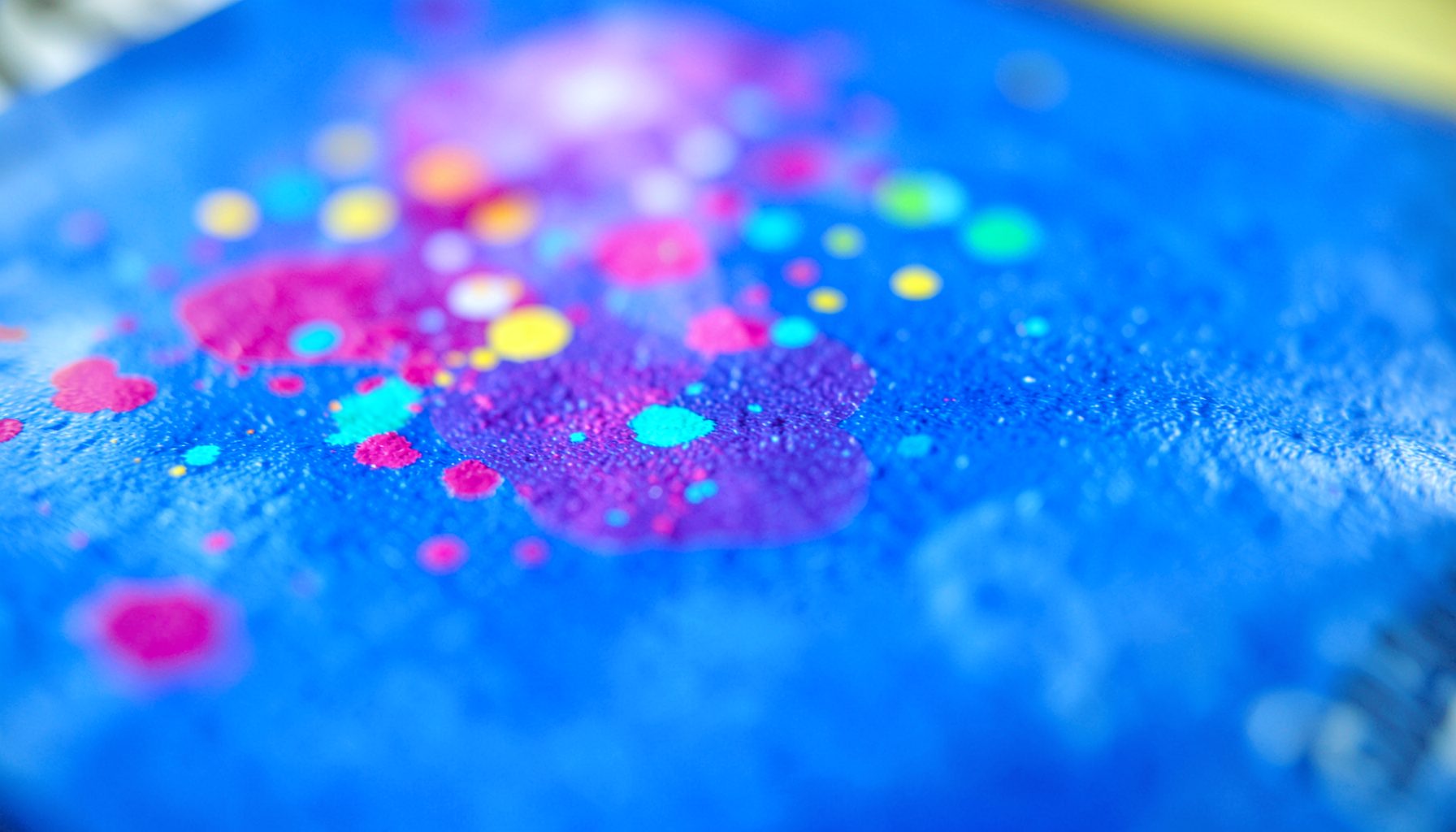 Extreme close-up of glossy magazine paper with vibrant ink dots in magenta, cyan, and yellow, soft diffused lighting