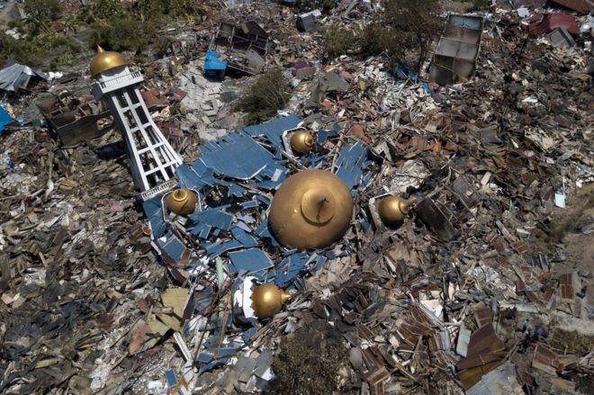 Aerial view of a collapsed building with domed roof structures amid piles of debris and rubble