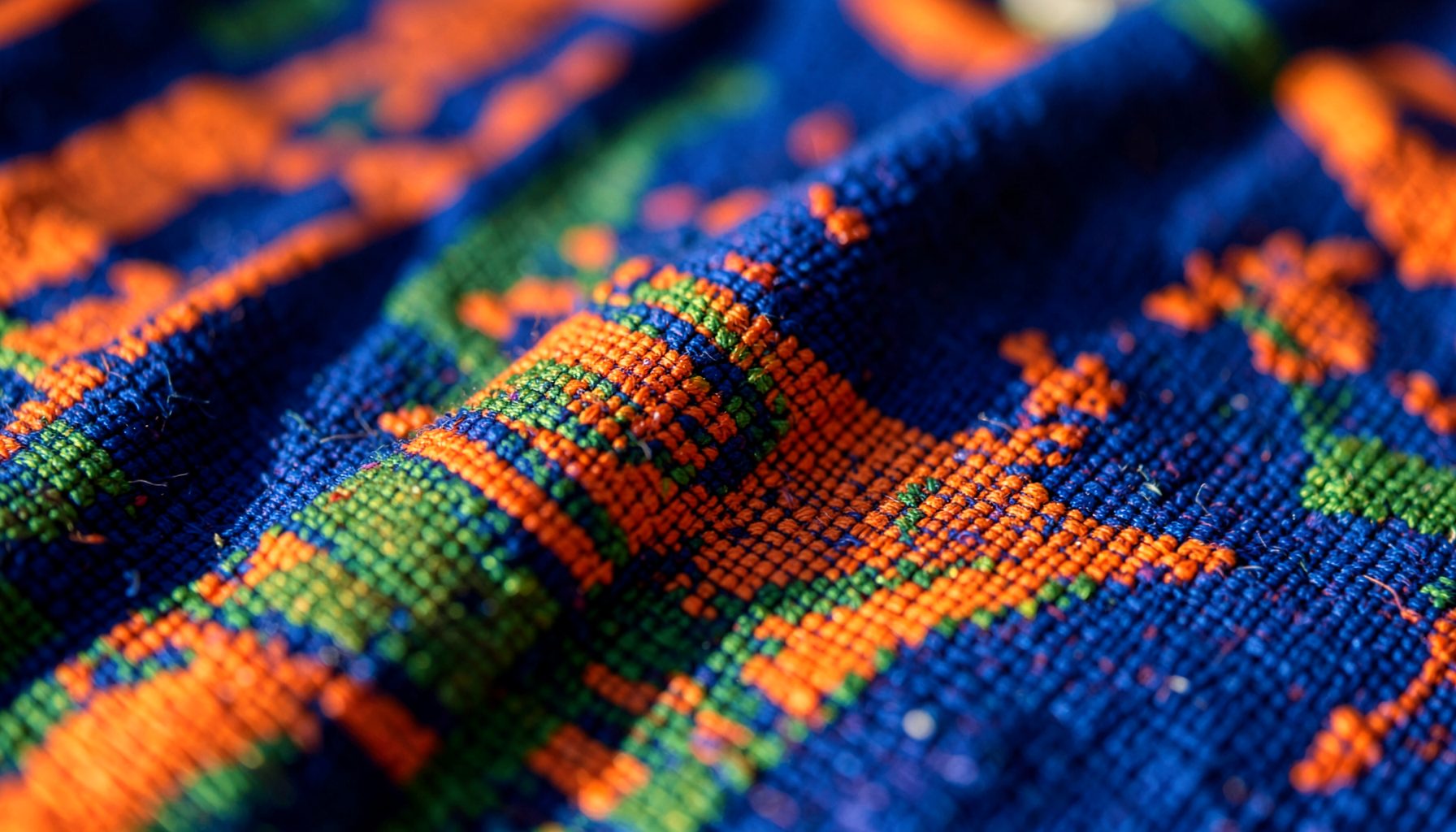 Close-up of woven kitenge fabric with bold orange, blue, and green geometric patterns in warm sunlight, representing Tanzanian trade and textiles