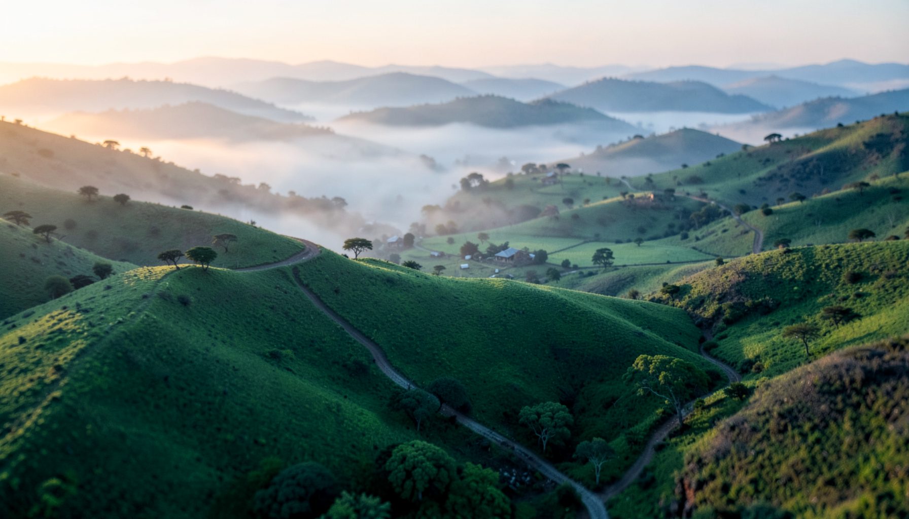 Aerial photograph of rolling green hills and border landscape at dawn, soft mist hanging in the valleys, evoking East African cross-border trade routes